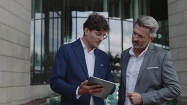 Tablet kullanan ve dışarıda konuşan iki iş adamı.