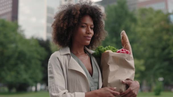 Mujer sonriente sosteniendo bolsa de comestibles mientras está de pie en la calle — Vídeo de stock