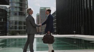 Takım elbiseli adamlar şehir merkezinde dururken el sıkışıyor.