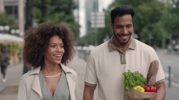 Pozitivní pár kráčí po ulici a nese nákupní tašku — Stock video