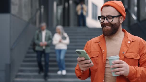 Hombre feliz llevando café y usando el teléfono celular al aire libre — Vídeo de stock