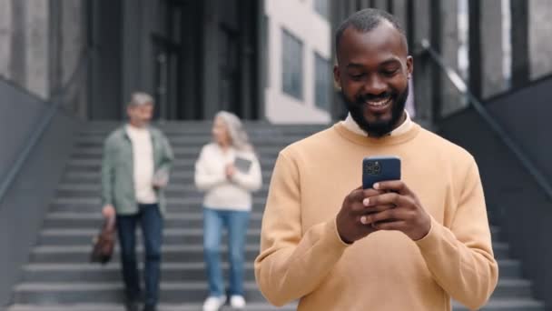 Gülümseyen Afro-Amerikan adam açık havada cep telefonu kullanıyor. — Stok video