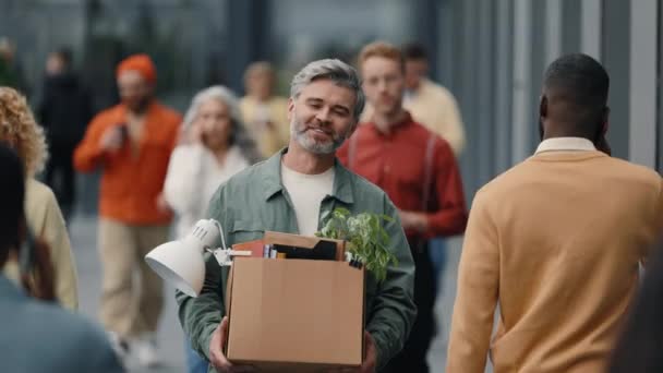 Happy aged man walking on busy street with box of stuff — Stockvideo