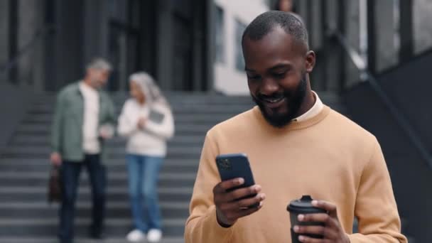 African american man using mobile and carrying coffee — Stok video