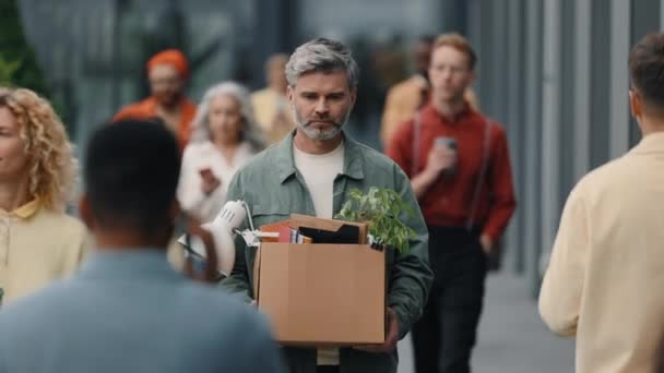 Sad man walking on busy street with box full of belongings — Stok video
