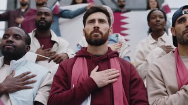 Elleri yüreğinde futbol maçında milli marşı dinleyen bir adam.