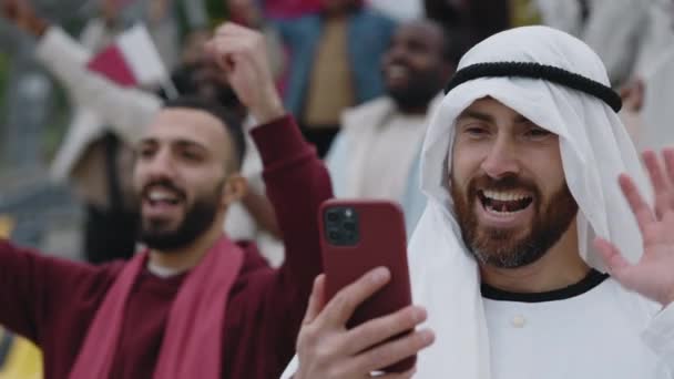 Man in sheikh outfit live streaming soccer game using mobile — Stockvideo