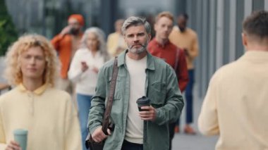 Successful grey haired man walking on busy urban street