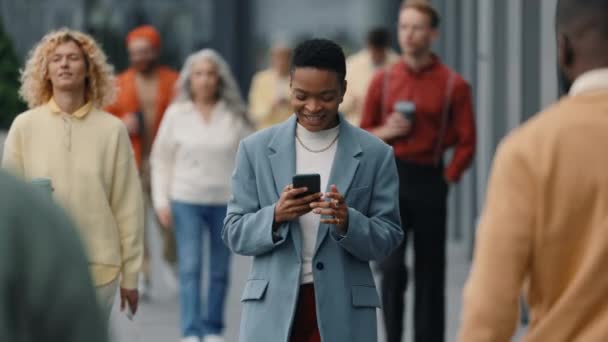 Щаслива бізнес-леді, що йде по вулиці і використовує мобільний — стокове відео