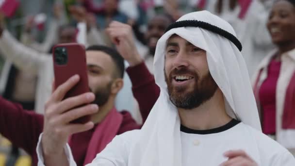 Arabian man having video call on mobile during soccer match — стокове відео