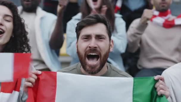 Mężczyzna trzyma włoską flagę i krzyczy podczas gry w piłkę nożną — Wideo stockowe