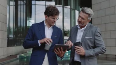 Businessmen holding coffee and using tablet outdoors