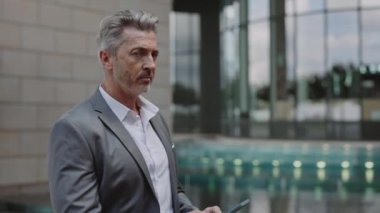 Aged man in suit holding mobile and looking at camera