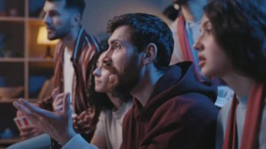 Sakallı erkek futbol fanatiği evinde, kanepede oturuyor ve arkadaşlarıyla televizyon programı yarışması şampiyonasını seyrediyor. Gergin insanlar favori takımı destekliyor ve gol bekliyorlar..