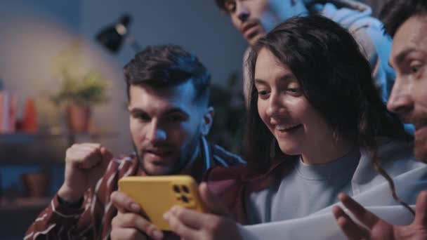 Positieve vrolijke mensen kijken naar de smartphone met blije emoties tijdens het voetballen. Spannende voetbalfans met behulp van moderne smartphone op thuis. Voetbalfans concept. — Stockvideo