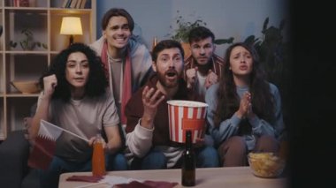 Gergin arkadaşlar maçta kaybettikleri için hayal kırıklığına uğradılar. İnsanlar TV 'de program izlerken spor takımı için tezahürat yapıyorlar ve yüksek sesle olumlu sonuçlar için umut ediyorlar.