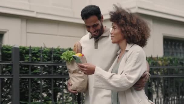 Familia feliz usando móvil y llevando bolsa de comestibles en la calle — Vídeos de Stock