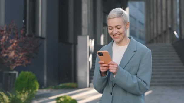 Smiling lady texting on smartphone while walking outdoors — Stock Video