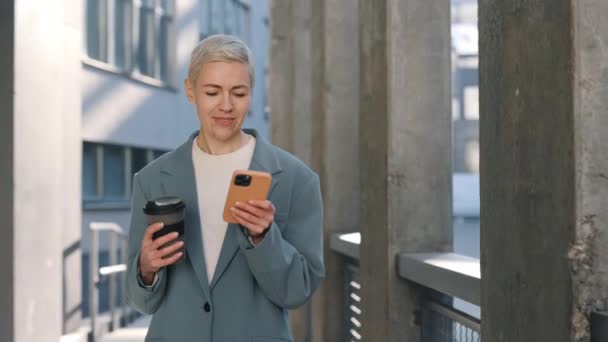 Žena držící kávu a pomocí mobilu v městské oblasti — Stock video