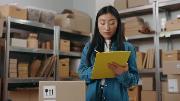 폴더를 들고 있는 아시아인 소녀의 초상화를 흔들고 고객에게 폴더를 보낼 준비를 하면서 소포에 대한 정보를 쓴다. 작은 사업 개념. — 비디오