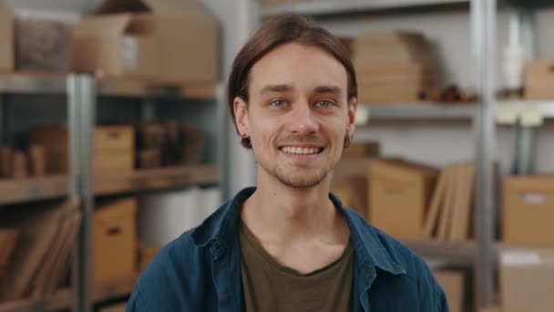 Knappe blanke man die aan tafel staat en poseert met pakjes bij de kast in zijn kantoor terwijl hij glimlacht naar de camera. Concept voor kleine ondernemingen. — Stockvideo
