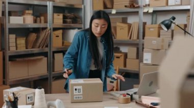 Masada duran esmer kadının belden yukarı portre görüntüsü ve iş yerinde hafif bir gülümseme ile paketlenmiş paketler. Küçük işletme kavramı.