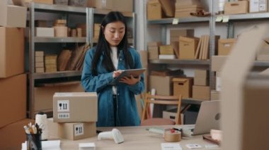 Tablet bilgisayarı tutan Asyalı kızın belindeki portre görüntüsünü kaldır ve paketle ilgili bilgileri kontrol et. Müşteriye göndermeye hazırlanırken. Küçük işletme kavramı.