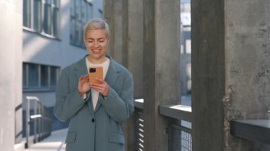 Resmi giyinmiş olgun bir bayan açık havada akıllı telefon kullanıyor.