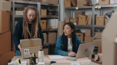 Asyalı meslektaşı laptopta çalışırken özel bir aletle paketleri tarayan beyaz kadının belindeki portre görüntüsünü kaldır. Küçük işletme kavramı.