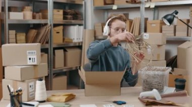 Dikkatli, dikkatli, kulaklık takan, iş yerinde oturan ve paketleri hafif gülücüklerle paketlerken kutuyu dolduran adamın portre görüntüsünü yükseltin. Küçük işletme kavramı.