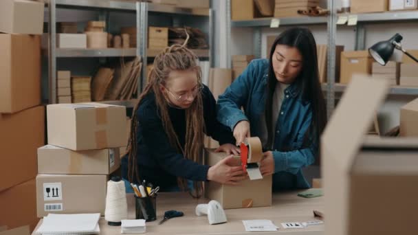 Las mujeres jóvenes propietarios de tiendas en línea sella paquetes con paquete de cinta, mientras que la preparación de la caja de paquetes de entrega en el almacén. Servicio postal y concepto de pequeña empresa. — Vídeo de stock