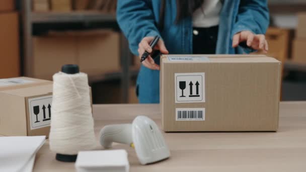 Pemandangan tentang perempuan Asia pemilik usaha kecil berdiri di meja dan menulis sesuatu di kotak lemari dengan ujung pena ketika mempersiapkan paket untuk pengiriman. — Stok Video