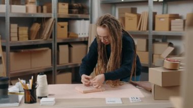 En sevdiğim iş. Kafkasyalı genç kadının belden yukarı portre görüntüsü. Depoda duran rastalı ve küçük pakette ip bağlayan kadın. Küçük işletme kavramı.