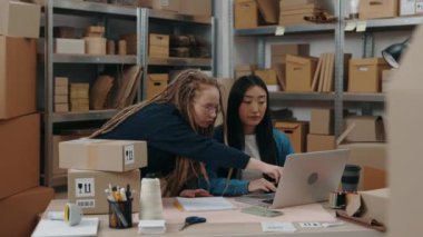 Beyaz kadın, Asyalı meslektaşı merkez büroda çalışırken bilgisayarın ekranını parmağıyla kapatıyor. Küçük işletme kavramı.