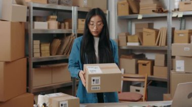 Uzun saçlı, gözlüklü, depoda duran ve elinde bir paket varken kameraya bakan kadının portre görüntüsünü yükseltin. Meslek kavramı.