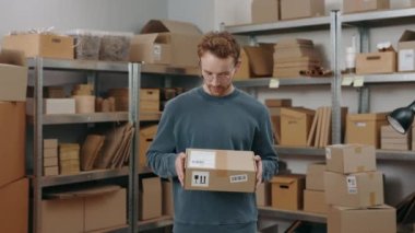 Küçük bir iş. Depoda durup elinde paket tutarken kameraya bakan şık gözlüklü adamın belden yukarı portre görüntüsü. Meslek kavramı.