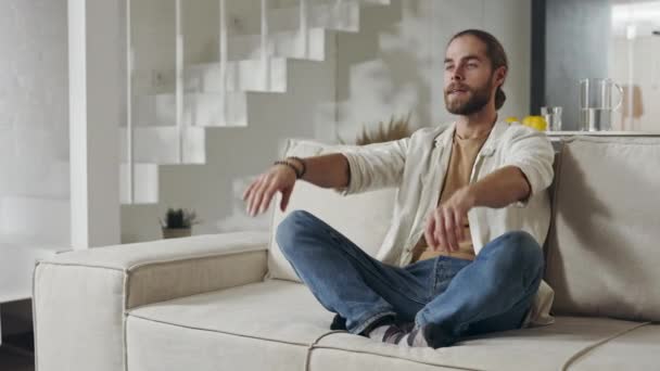 Bonito homem meditando no sofá em pose de lótus — Vídeo de Stock