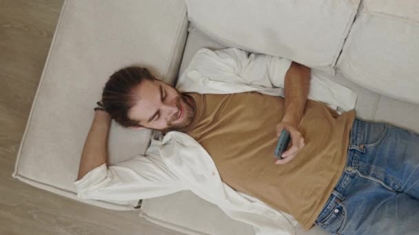 Счастливый парень лежит на диване со смартфоном в руках — стоковое видео