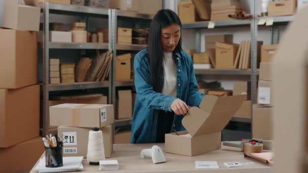 Cintura arriba retrato vista de la mujer morena asiática de pie en la mesa y poniendo poco paquete en la caja del armario mientras trabajaba en la oficina en casa. Concepto empresarial. — Vídeo de stock