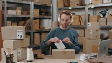 Dükkan sahibi. Kafkasyalı kızıl adam depoda çalışırken paketin üzerine müşteri adresi etiketleri yapıştırıyor. Posta servisi ve küçük işletme kavramı.