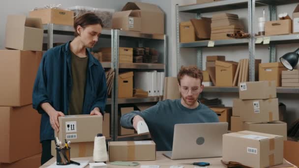 Vista de la cintura hacia arriba del retrato del hombre caucásico y su colega masculino escaneando el código de barras en la caja del armario mientras prepara la caja de paquetes de entrega. Servicio postal y concepto de pequeña empresa. — Vídeos de Stock