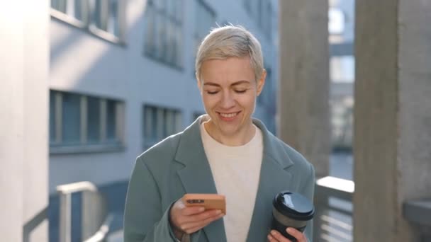 Happy starší dáma nesoucí kávu a pomocí mobilní na ulici — Stock video