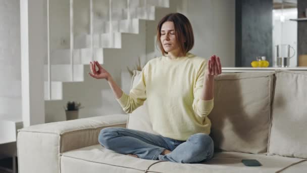 Mulher meditando na posição de lótus no sofá confortável — Vídeo de Stock