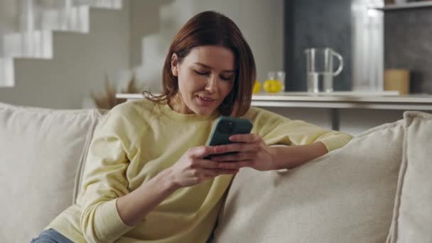Kanepede oturan mutlu kadın elinde akıllı telefonuyla — Stok video