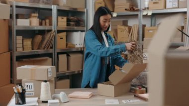 Depoda duran Asyalı kadının portre görüntüsünü belden yukarı kaldırın ve ahşap masaya paket paketlerken dolap kutusuna dolgu koyun. Küçük işletme kavramı.