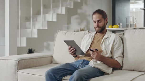 男人坐在沙发上，拿着平板电脑和银行卡 — 图库视频影像
