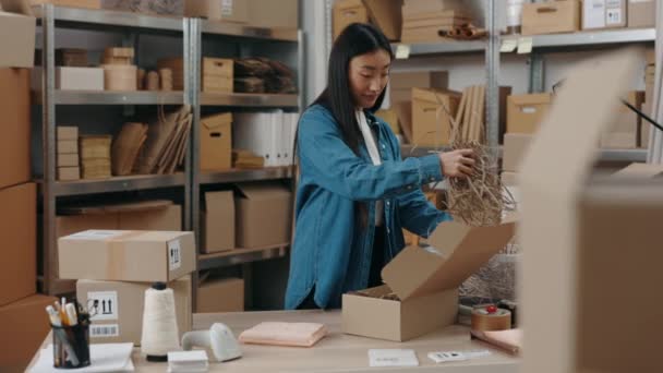 창고에서 있는 아시아인 여인의 초상화를 흔들어 보고 나무 식탁에 꾸러미를 싸고 찬장에 채워 넣는 모습을 상상 해 보라. 작은 사업 개념. — 비디오