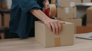 Beyaz adamın masada dikilip koli bandıyla paket paketlediği görüntüler. Posta servisi ve küçük işletme kavramı.