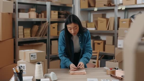 Dikkatli işçi. Modayı takip eden modern Asyalı bayanın belden yukarı portre görüntüsü. Ofisinde duruyor ve el işi kağıdında paket paketliyor. Kız ipi. Küçük işletme kavramı. — Stok video