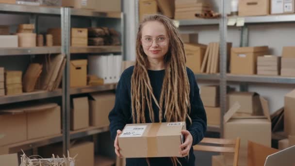 Çekici beyaz kadın, uzun saçlı, masada duruyor ve kameraya gülümserken dolaptaki kutularda poz veriyor. Küçük işletme kavramı. — Stok video
